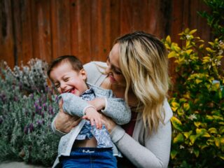 woman in gray sweater carrying baby in blue and white shirt