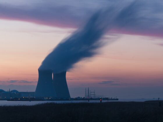 skyline photography of nuclear plant cooling tower blowing smokes under white and orange sky at daytime