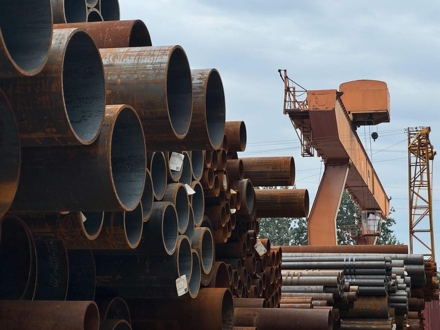 Stacked steel pipes beside an industrial crane in an outdoor yard, showcasing heavy industry and construction materials.