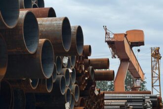 Stacked steel pipes beside an industrial crane in an outdoor yard, showcasing heavy industry and construction materials.